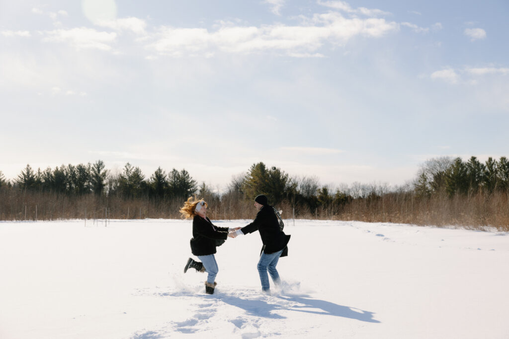 Couple running around in the snow in a field