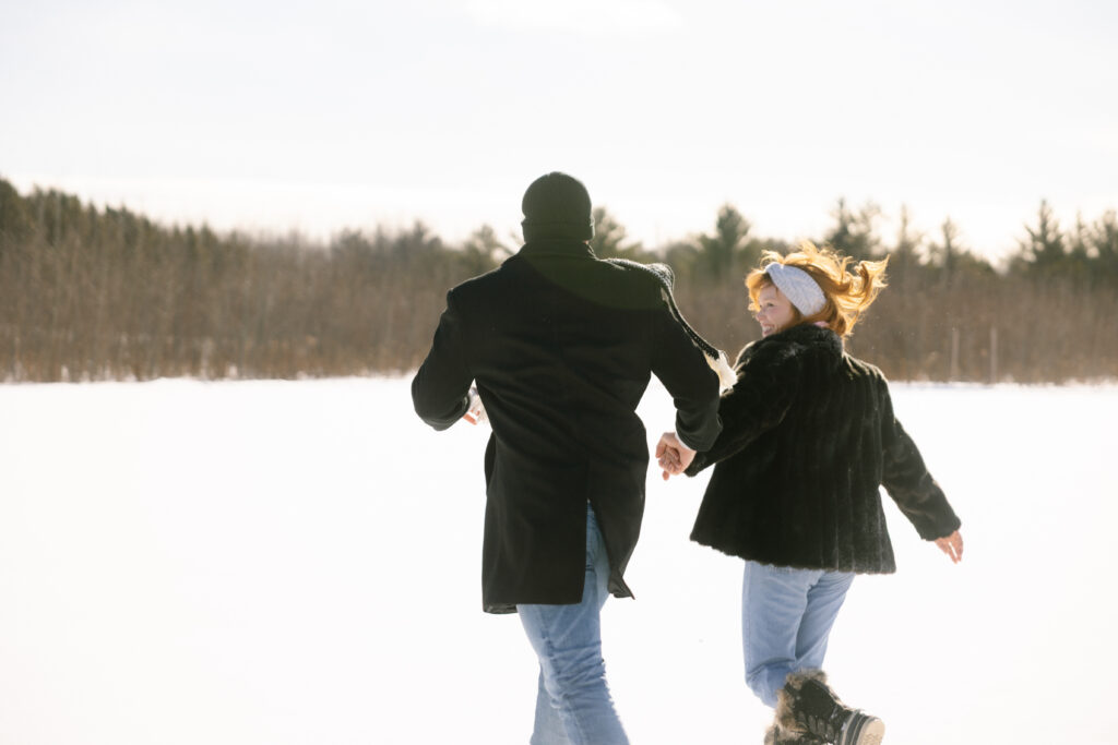 Couple running around in the snow in a field