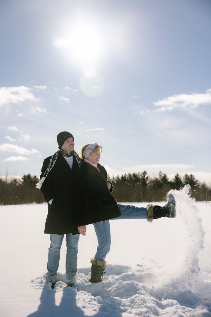 Couple standing side by side kicking snow