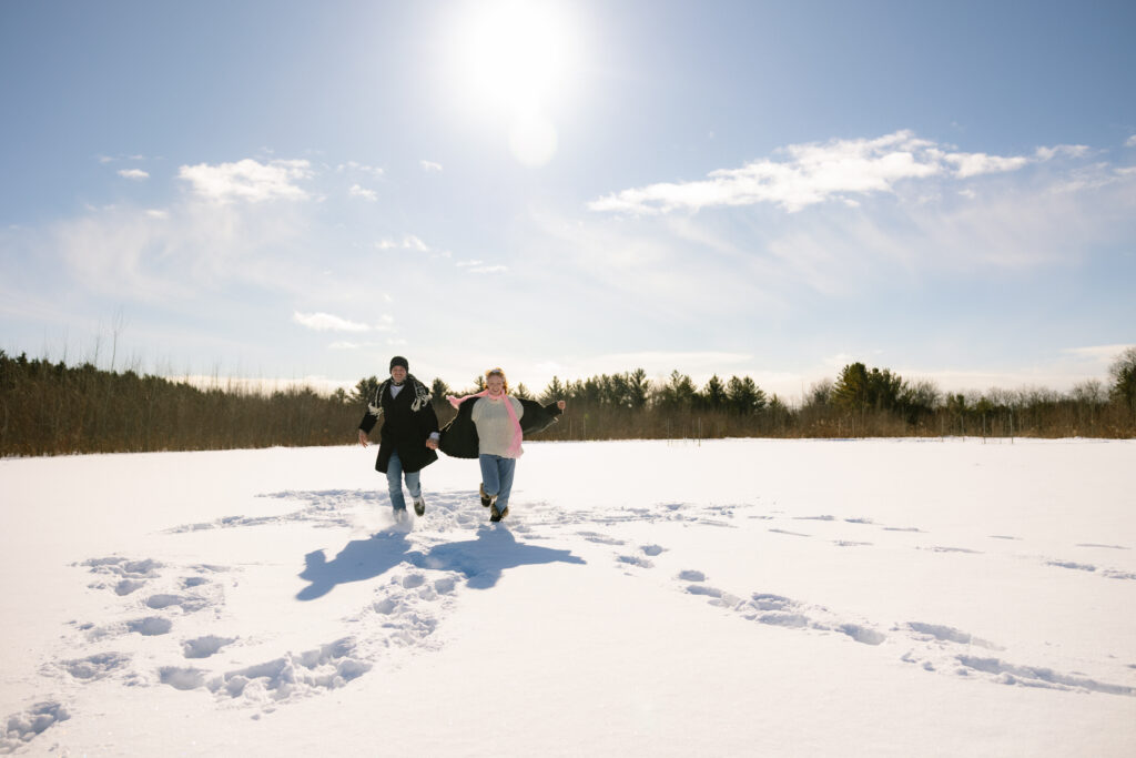 Couple running around in the snow in a field