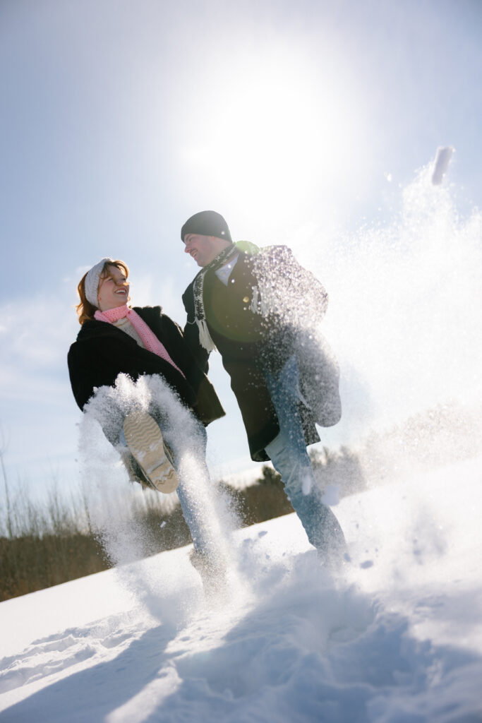 Couple standing side by side kicking snow