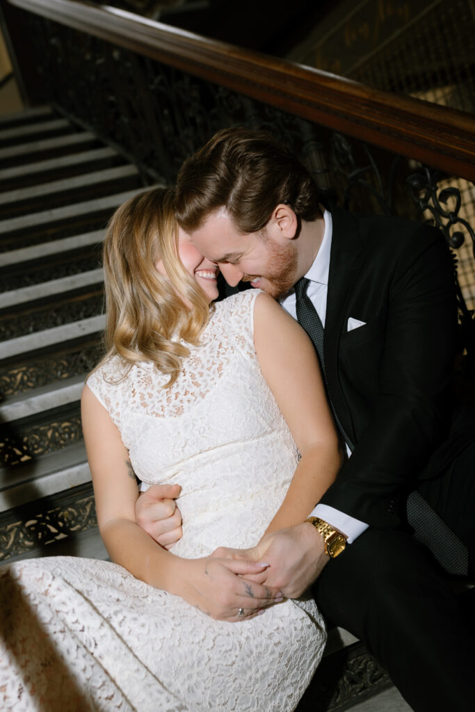 Toronto Old City Hall Civil Ceremony Couple sitting on stairs while nuzzled into her shoulder