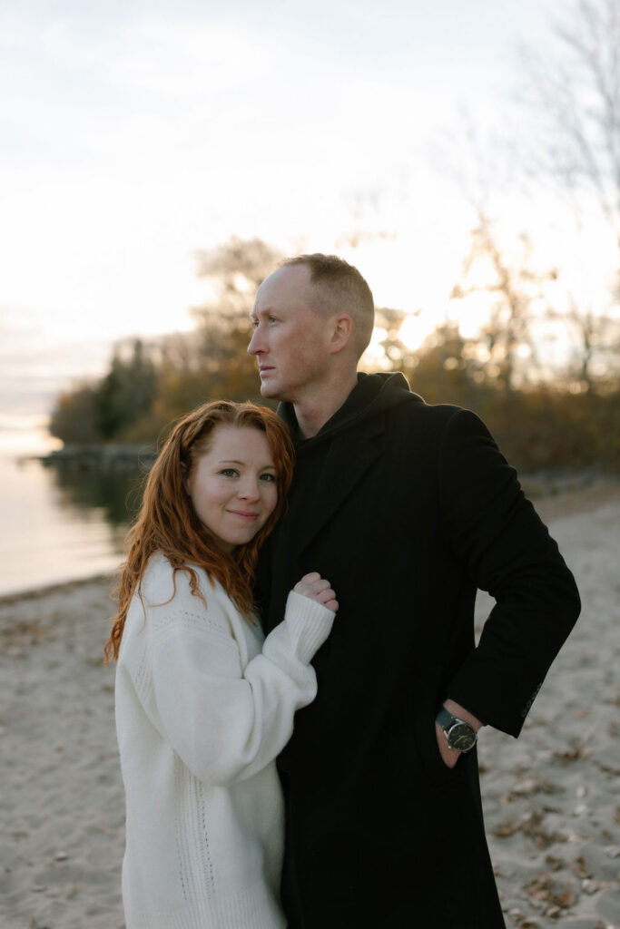 Toronto Island proposal couple cuddling on the beach and looking out to the water